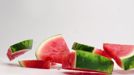 rodajas de sandía rosa brillante y fresca con corteza verde que cae sobre la mesa blanca con gotas de jugo rociadas a cámara lenta