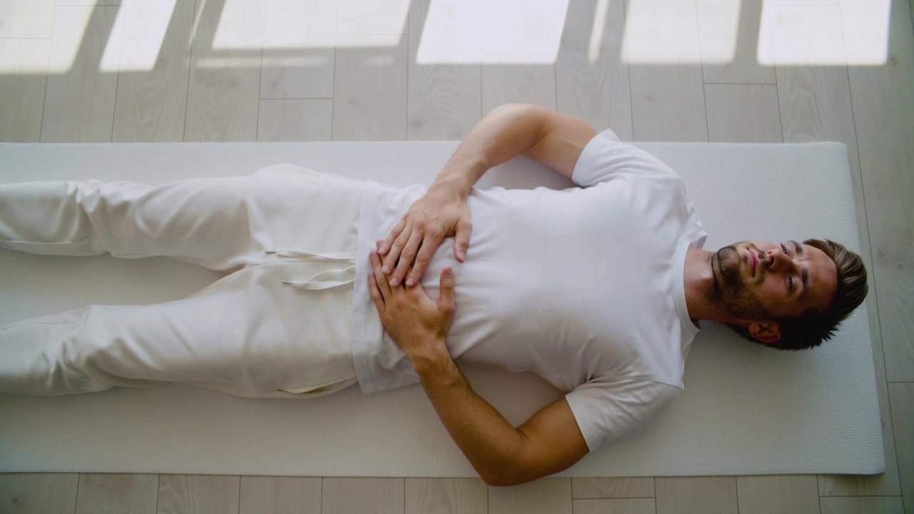Starting man resting on home mat, breathing with hands on belly for relaxation wearing white tee