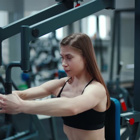 sports girl in a black top and leggings performs an exercise on his chest simulator in a fitness club. blurred background