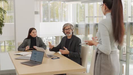 two modern elegant economists looking at their female colleague during discussion of graphic financial data at meeting in office