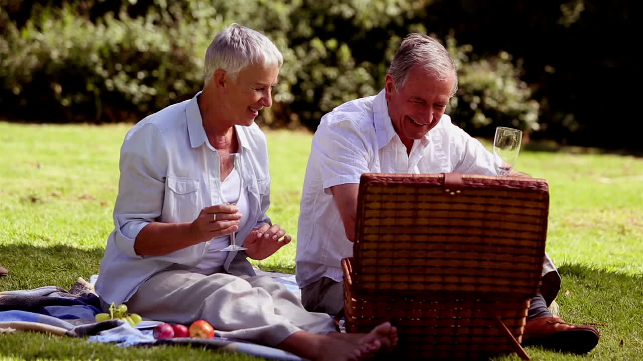 una pareja madura haciendo un picnic con vino blanco.
