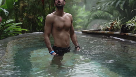 el hombre mira las copas de los árboles mientras está en una piscina de lujo en la selva tropical, a cámara lenta