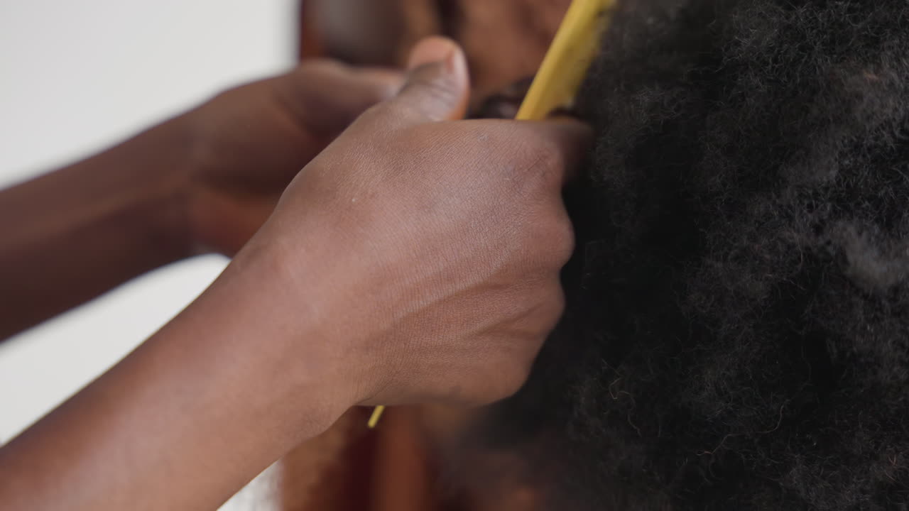 Mani nere che misurano i capelli con un pettine giallo, stilista che esegue un'attenta sezionatura e trecciatura su texture afro naturale, primo piano di dita e cuoio capelluto, sessione di toelettatura concentrata in uno studio calmo, dettagliata.