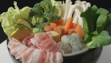 close up of a pot of shabu ingredients spinning around on white table in the black background kitchen