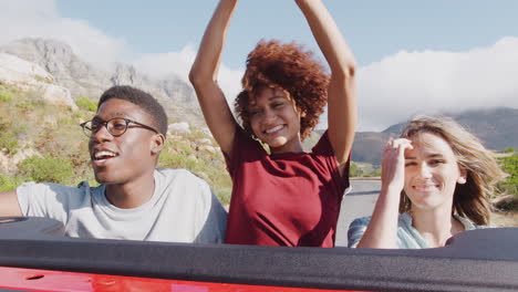 group of young friends standing up in back of open top hire car on summer vacation