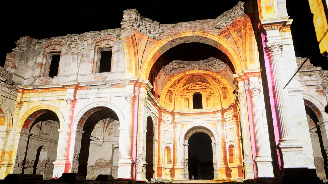 Facciata in pietra che si illumina di notte, con luce arancione e bianco pallido cangiante, in risposta a proiezioni.