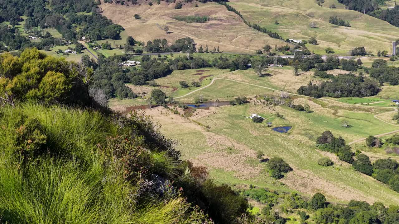 Aerial footage of lush green hills and rocky cliffs under bright sunlight in Nimbin, NSW, Australia