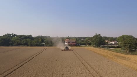 harvest claas combine harvester cropping towards camera with houses trees