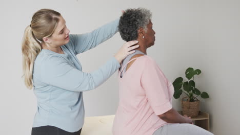 caucasian female physiotherapist checking neck of senior woman, copy space, slow motion