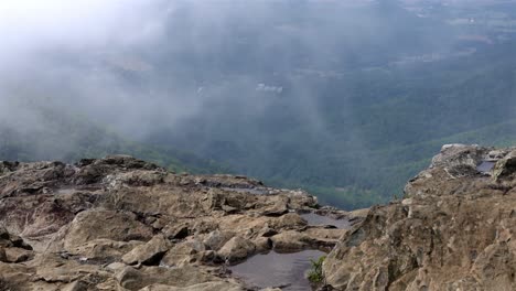 Handheld-static-shot-from-a-craggy-mountaintop-captures-wind-driven-movement-of-low-clouds-and-rippling-puddles