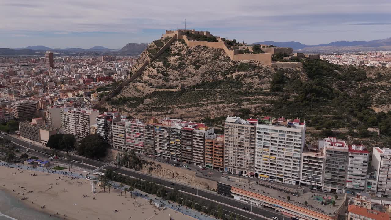 Aerial drone footage of Santa Bárbara Castle on Mount Benacantil overlooking Alicante and Playa del Postiguet. Mediterranean coastline and dense city skyline on the Costa Blanca in Spain