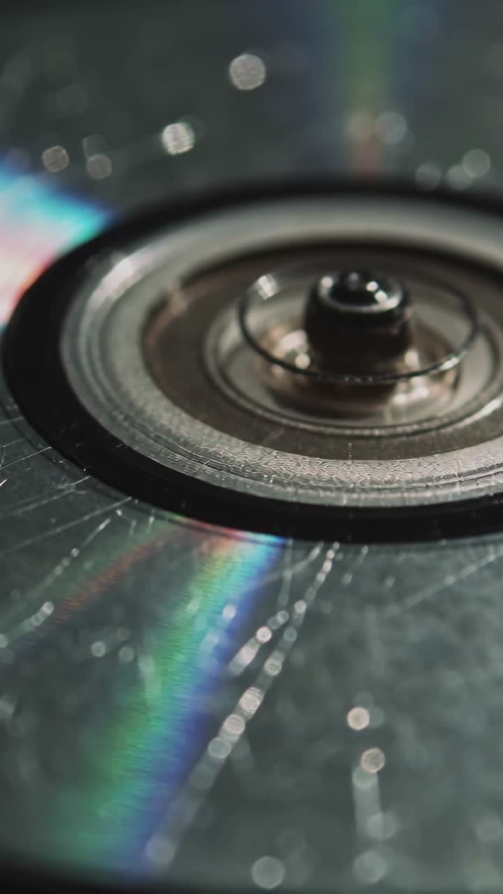 Vertikal video: Trækker fokuslinse over CD-nav på bænk for at inspicere ridser, viser regnbueglimt