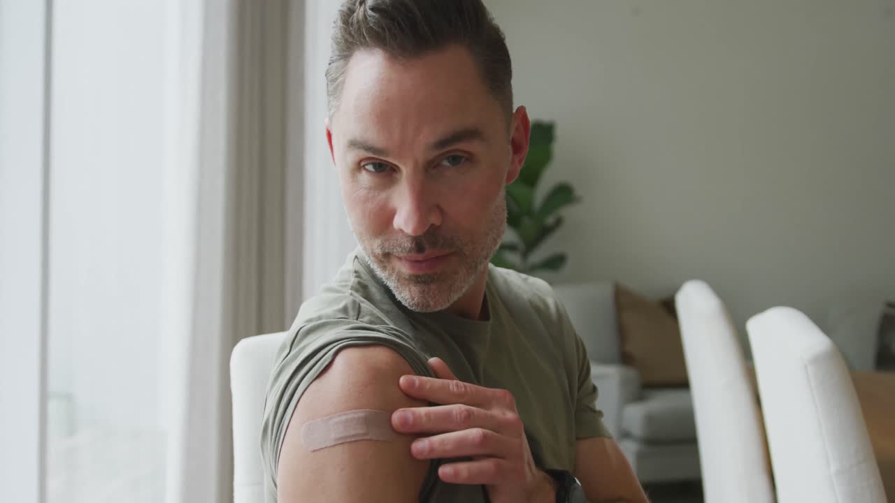 retrato de un hombre caucásico con hombro vacunado sonriendo y mostrando el signo ok en casa