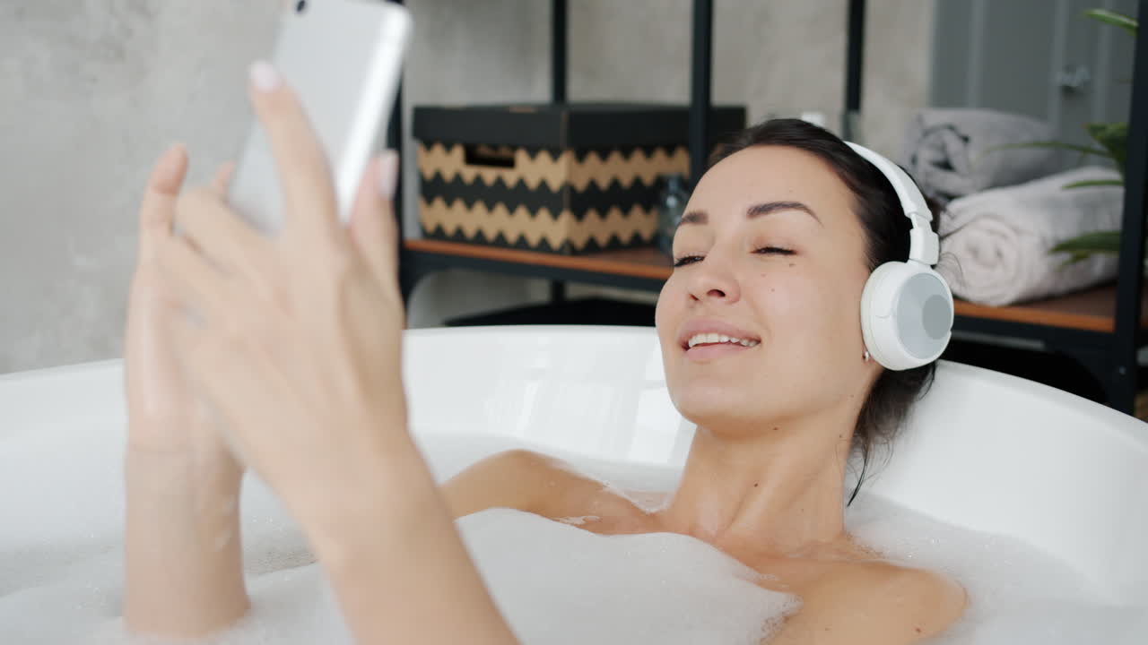 Woman Relaxing in a Bathtub with Headphones and Phone