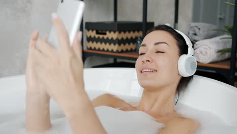 woman relaxing in a bathtub with headphones and phone