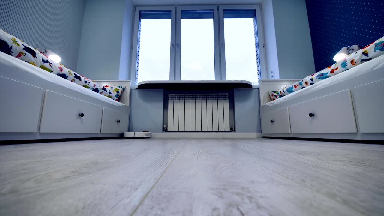un robot aspirador limpia entre las camas de dos niños en un hogar inteligente.