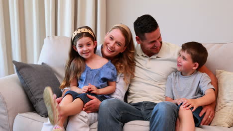 Happy-young-family-sitting-on-sofa-smiling-at-camera