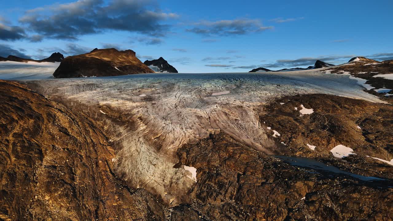 Likainen jäätikkökieli sedimenttikerroksineen ja uurteineen virtaa nunatakkien välissä auringonlaskussa, Norjassa, dronen kuvaamana.