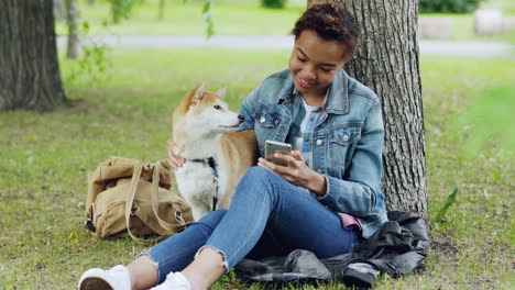 young woman with dog in park using smartphone