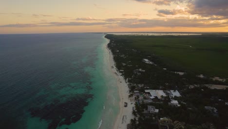 Vista-Aérea-De-La-Playa-De-Arena-De-Akiin-Con-Olas-Turquesas-Del-Mar-Caribe-Y-El-Cielo-Naranja-De-La-Puesta-De-Sol-En-El-Horizonte