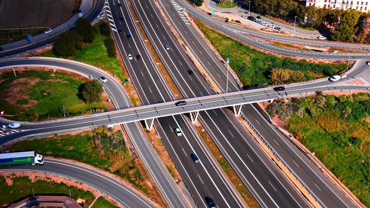 Cruce de carreteras complejo con múltiples carriles, pasos elevados y una pasarela peatonal de madera rodeada de vegetación. Vista aérea de intercambiador de autopistas y puente