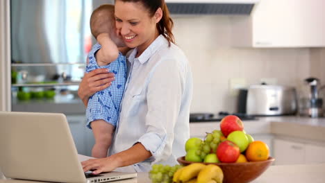 Pretty-mother-using-laptop-and-holding-baby