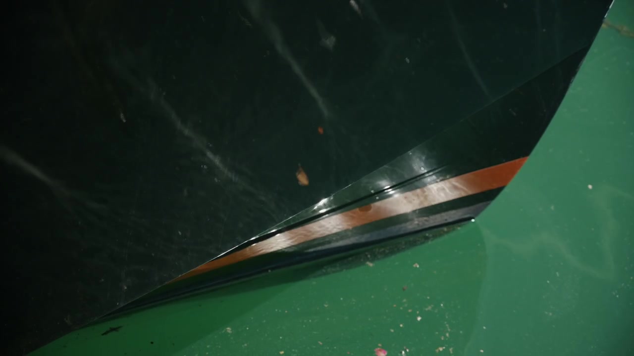 Elegante Nahaufnahme eines dunklen Yachtrumpfes, der sich auf ruhigem grünem Meerwasser in einem Yachthafen spiegelt.
