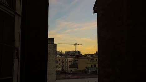 Gerahmte-Aufnahme-Des-Sonnenuntergangs-über-Einer-Baustelle-Im-Zentrum-Von-Valencia,-Gerahmt-Mit-Einer-Dunklen-Gasse,-Damit-Sie-Nach-Einbruch-Der-Dunkelheit-Aufleuchtet,-Atemberaubender-Zeitraffer