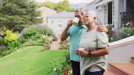 video de una relajada pareja de ancianos biraciales bebiendo café en el jardín