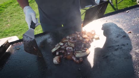 man tossing grilled onions with spatulas on hot grill in slow motion, close up, pull away for backyard bbq with friends