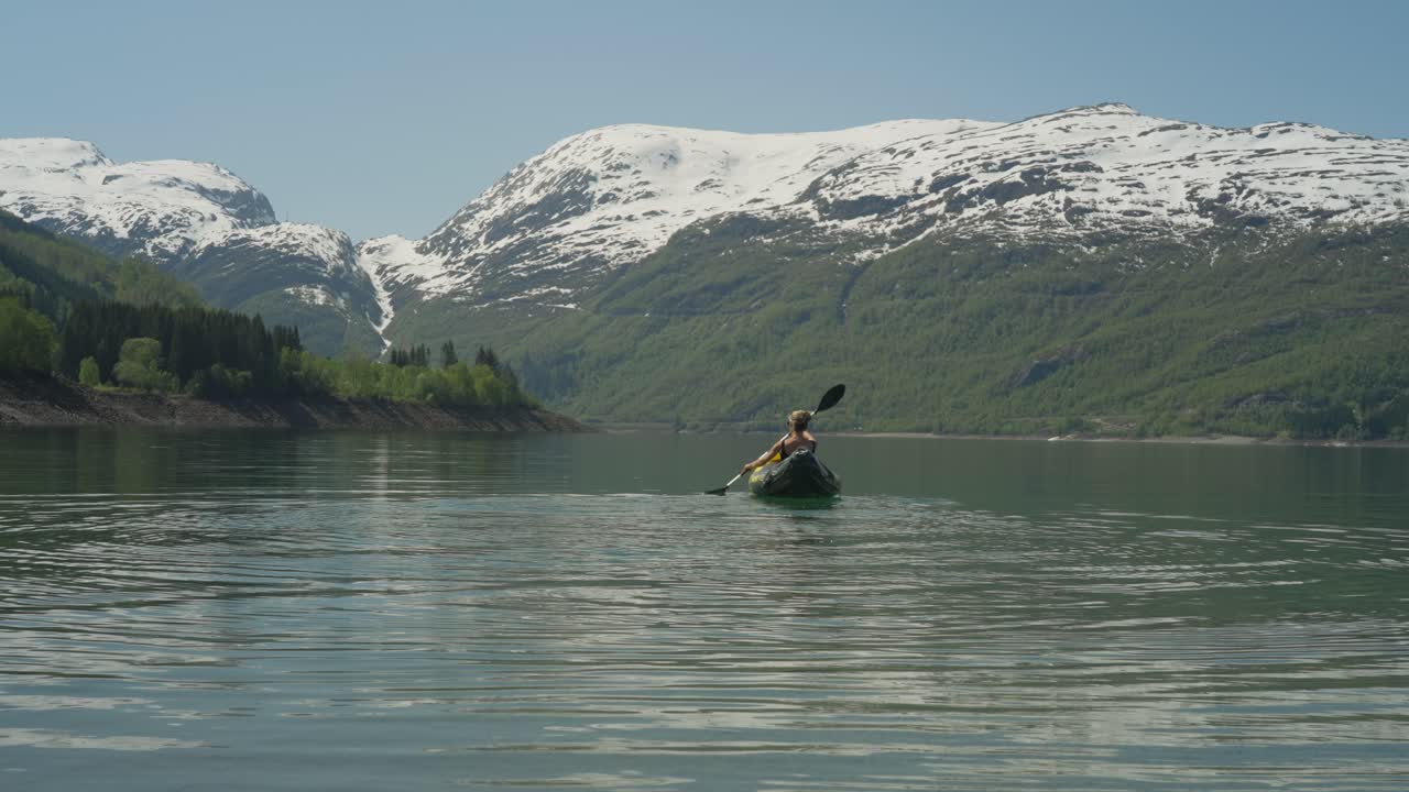 Kayaker paddling on a serene fjord with snowy mountains in Røldal, Norway