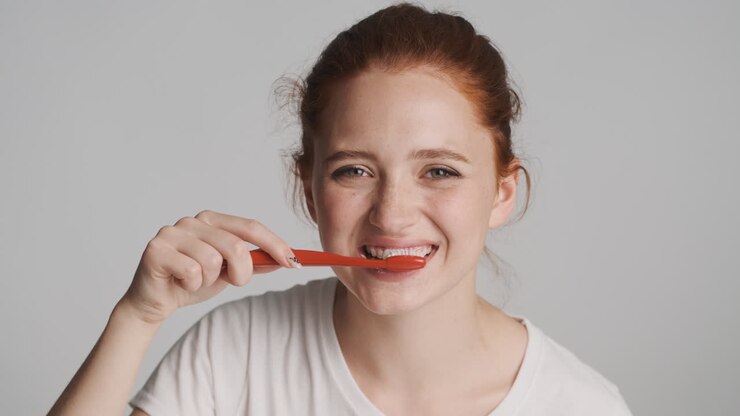 Redheaded girl in front of camera on gray background.
