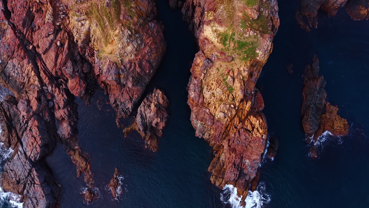 Rocce costiere colorate in acque profonde. Formazioni frastagliate multicolore incontrano il mare scuro e limpido in una vista aerea verticale