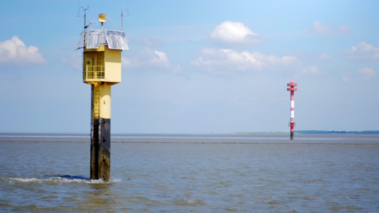 Leading lights standing in the water in the wadden sea, with a blue sky and clouds. Camera panning movement.