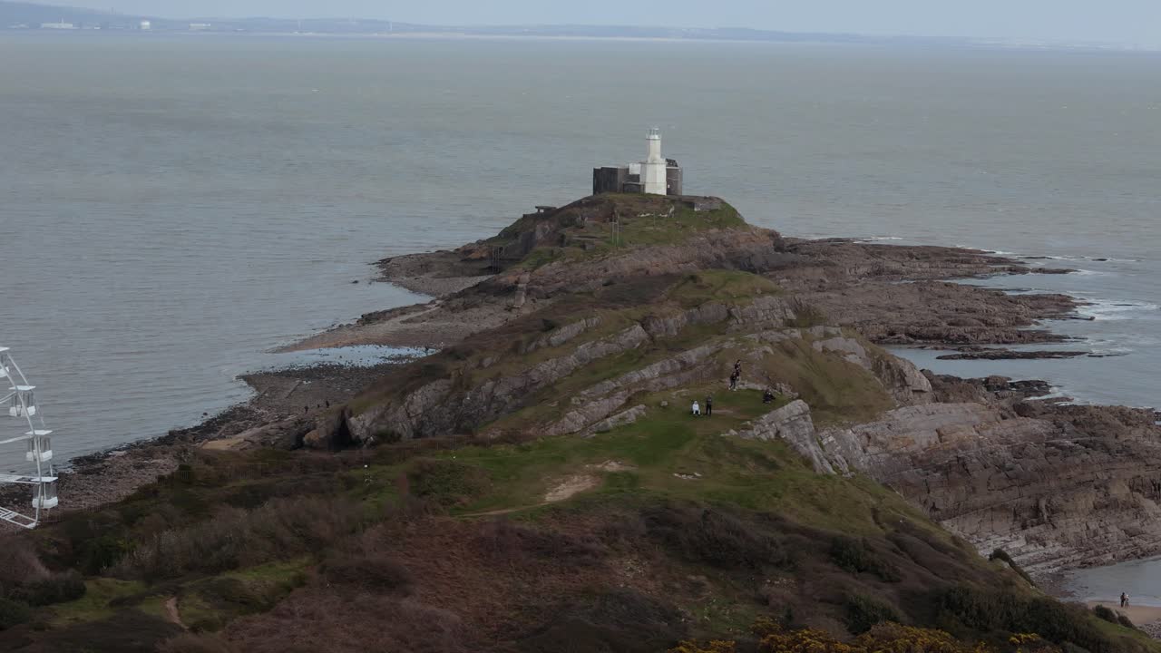 Aerial shot of The Big Wheel rotating at Mumbles Pier Swansea with a lighthouse at background in United Kingdom.