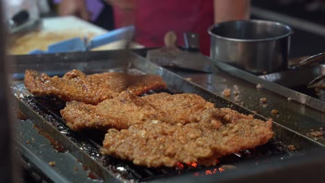 honey soy coated delicious fried chicken fillet grilling on hot grill, professional chef brush tasty sauce on the meat and flip side with a pair of tongs at famous night market, taiwan, asia