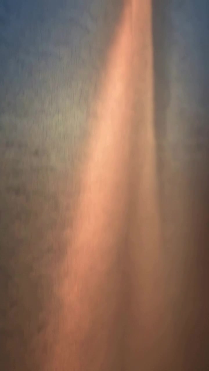 Vídeo vertical: Luz em movimento criando uma faixa quente que se move para a direita e se estreita na parede, revelando a borda