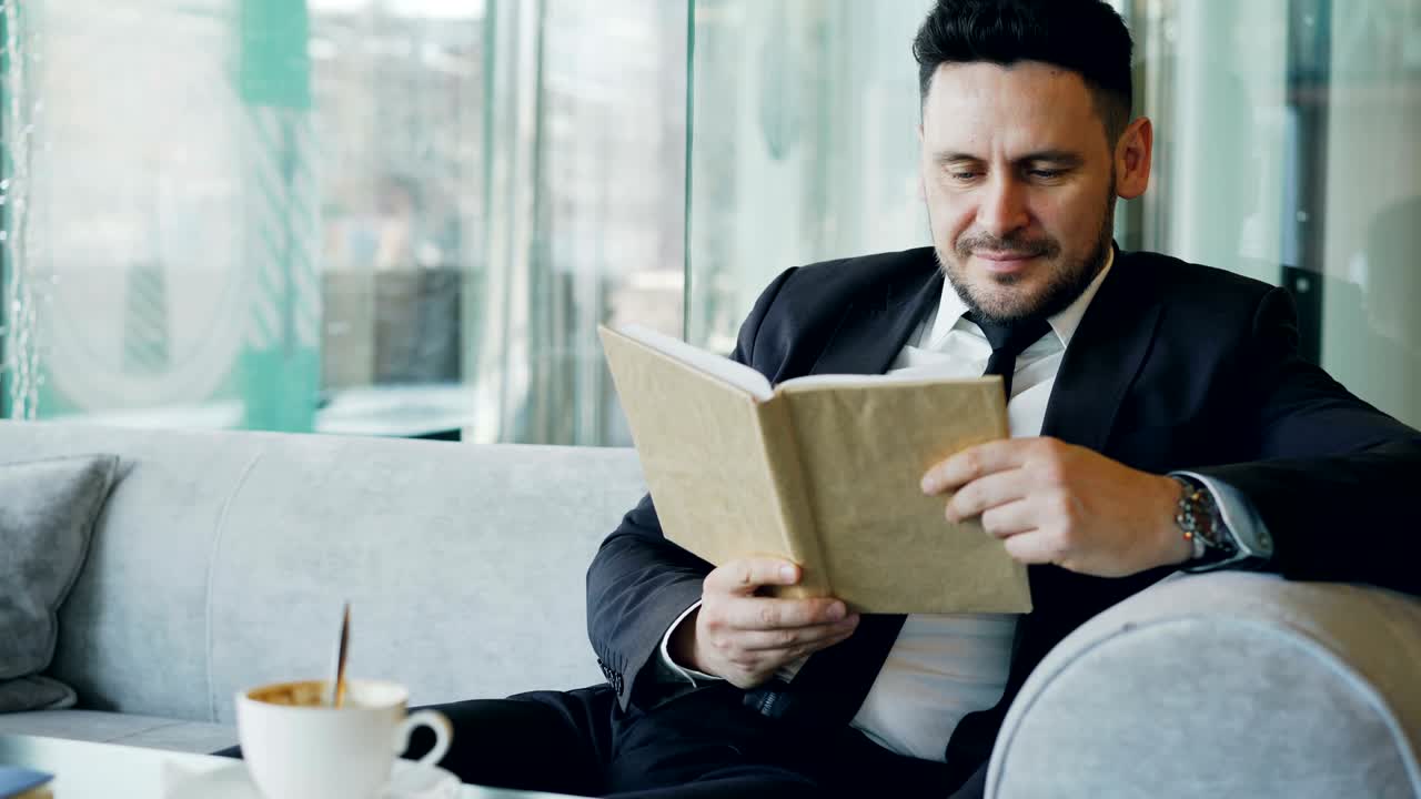 Empresário caucasiano inteligente em roupas formais lendo livro de texto e bebendo café no café elegante na hora do almoço
