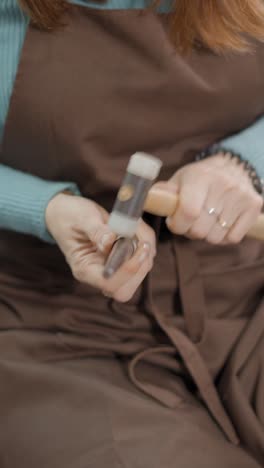 close-up of a person's hands crafting with a mallet and tool