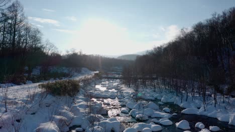 A-serene-winter-river-scene-in-Iwanai,-Hokkaido-with-snow-covered-banks-and-bright-sunlight