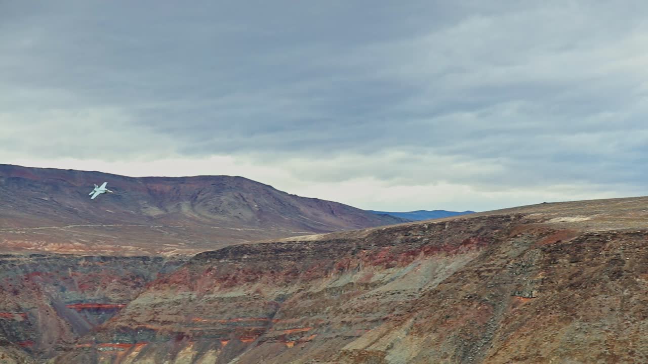 cámara lenta, vista de primer plano de un avión de combate que vuela a través de un cañón colorido, nivelándose desde la orilla derecha