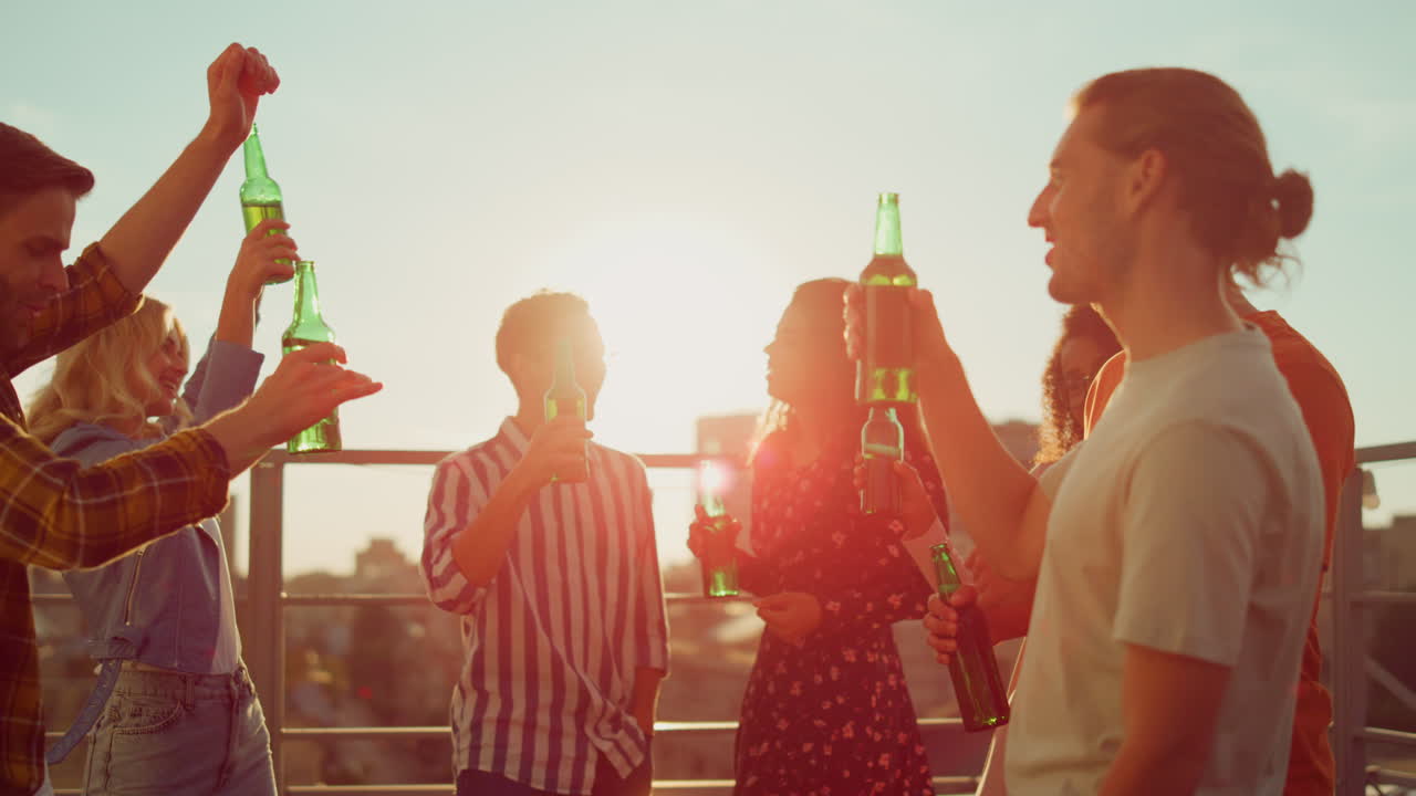 Smiling friends toasting with beer on terrace. Multiethnic people dancing party