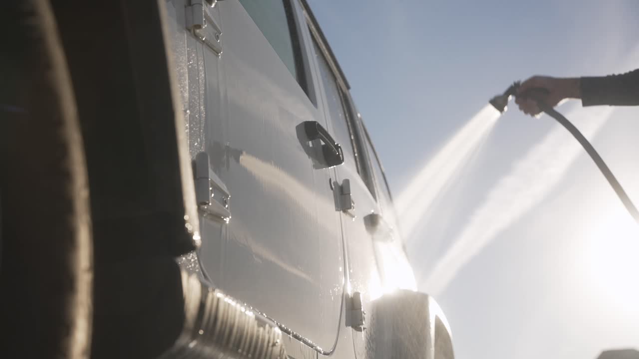 Sunlit water spray rinses the side of an SUV during an exterior wash