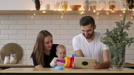 family of mother, father and baby sitting at home with a tablet pc