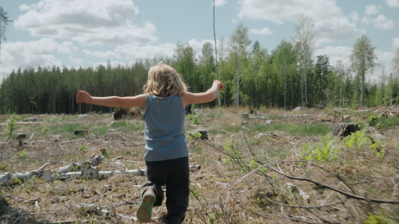 Energetic child runs into clearcut tract of land in woodland area, follow-cam