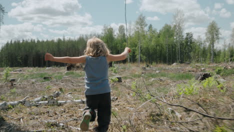 energetic child runs into clearcut tract of land in woodland area, follow-cam