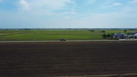 Pickup-truck-sideways-follow-and-reveal-drone-shot-surrounded-with-green-paddy-fields