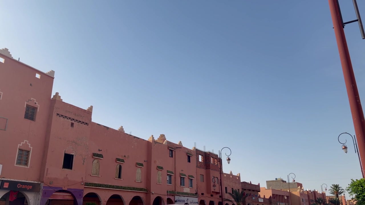 Fila di edifici stradali marocchini con archi e facciate rosa pastello sotto un cielo sereno.