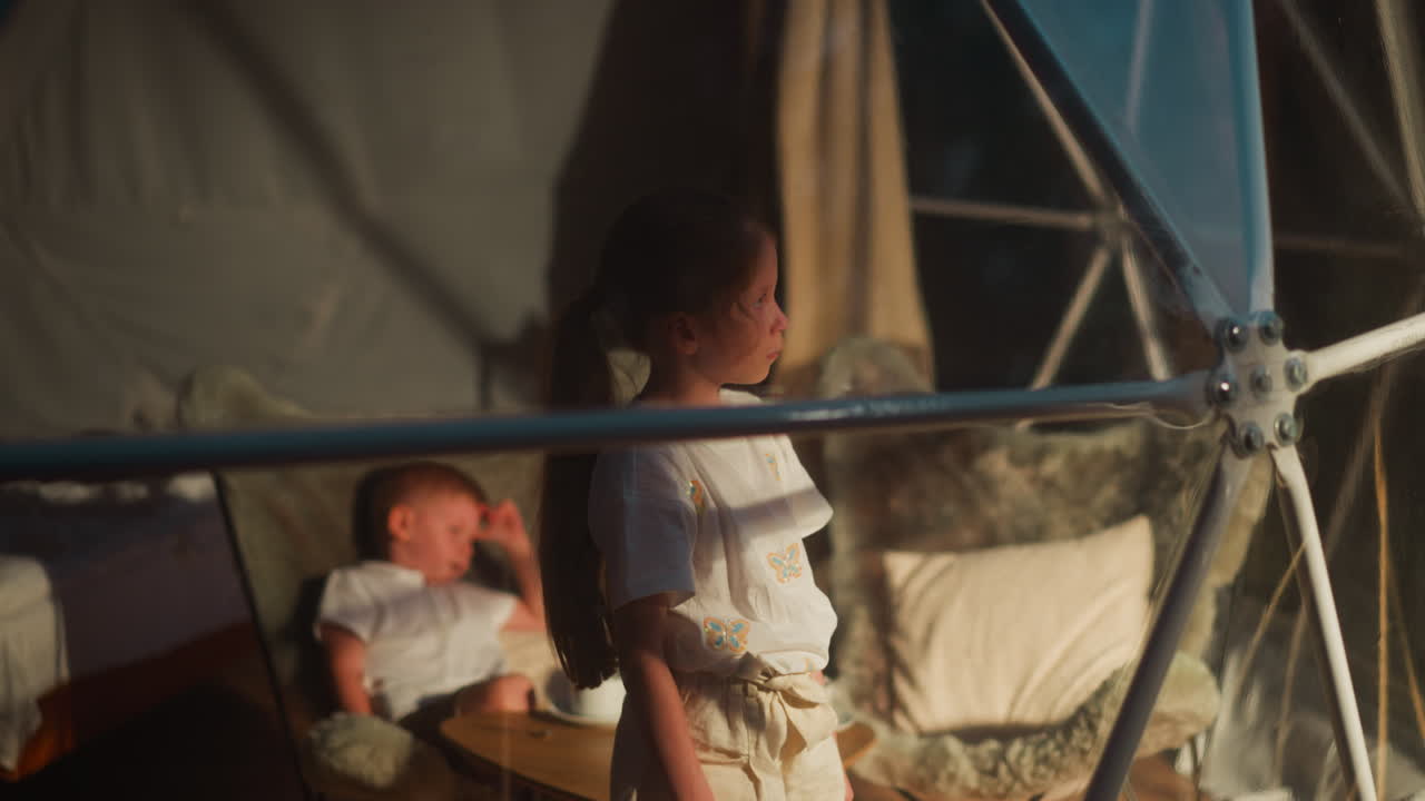 Upset little girl and sleepy brother in glamping hut. Children tired after active tourist day rest at luxury camp. Kids wait for parents in hotel room