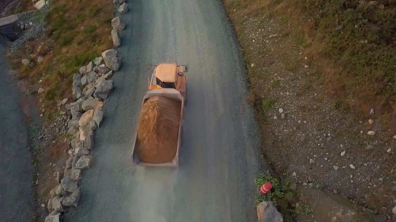 Fully loaded dump truck leaves construction. site dirt road and continues onto a paved road.
